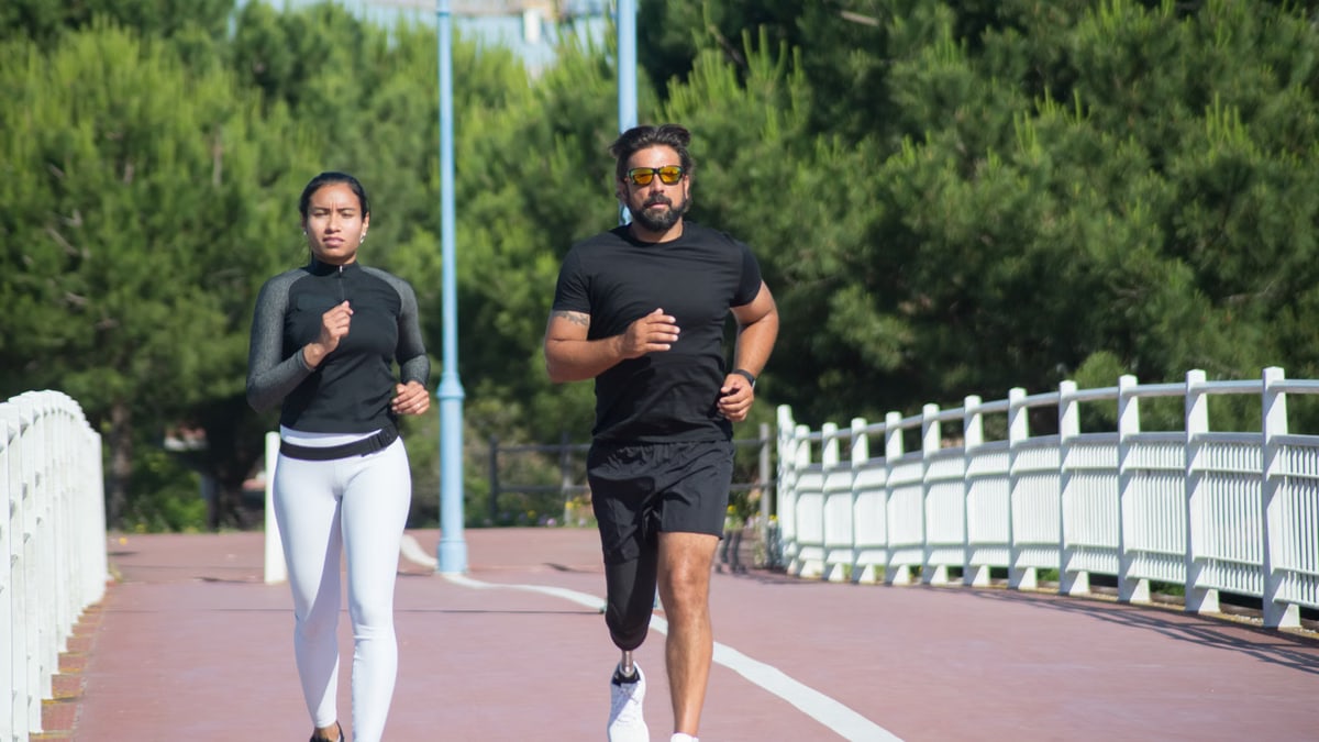 A couple jogging on a tree-lined path, enjoying an outdoor workout on a sunny day.
